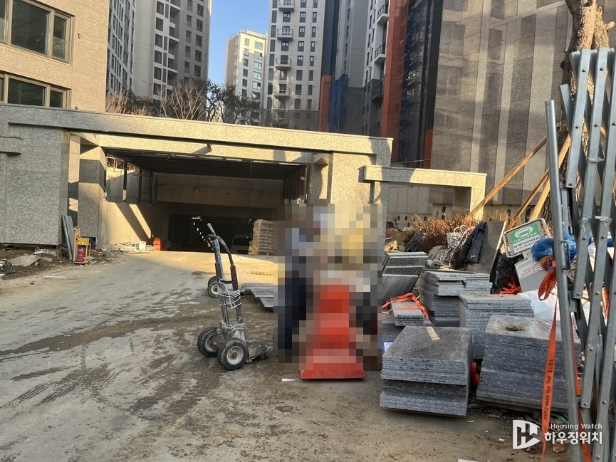 주차장 출입구 앞 가득 쌓여 있는 건설 자재를 작업하고 있는 하청업체 직원의 모습